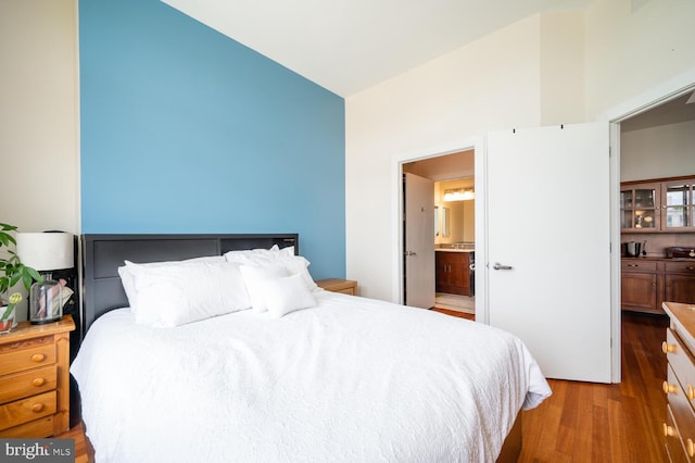 bedroom featuring hardwood / wood-style flooring, lofted ceiling, and ensuite bathroom