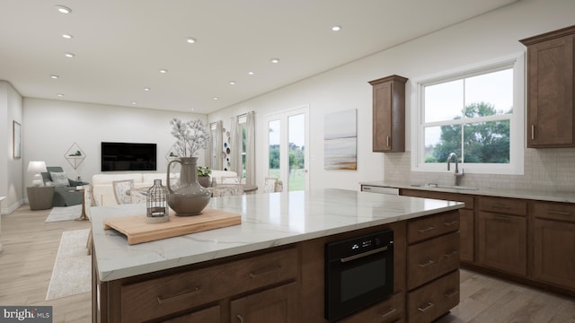 kitchen featuring light stone countertops, sink, backsplash, light hardwood / wood-style floors, and black oven