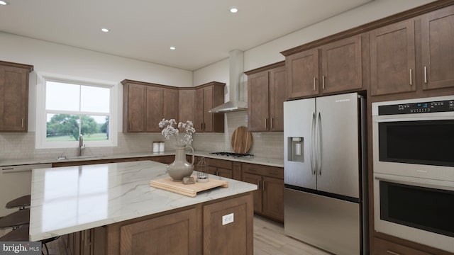 kitchen with appliances with stainless steel finishes, backsplash, a kitchen breakfast bar, light stone counters, and wall chimney exhaust hood