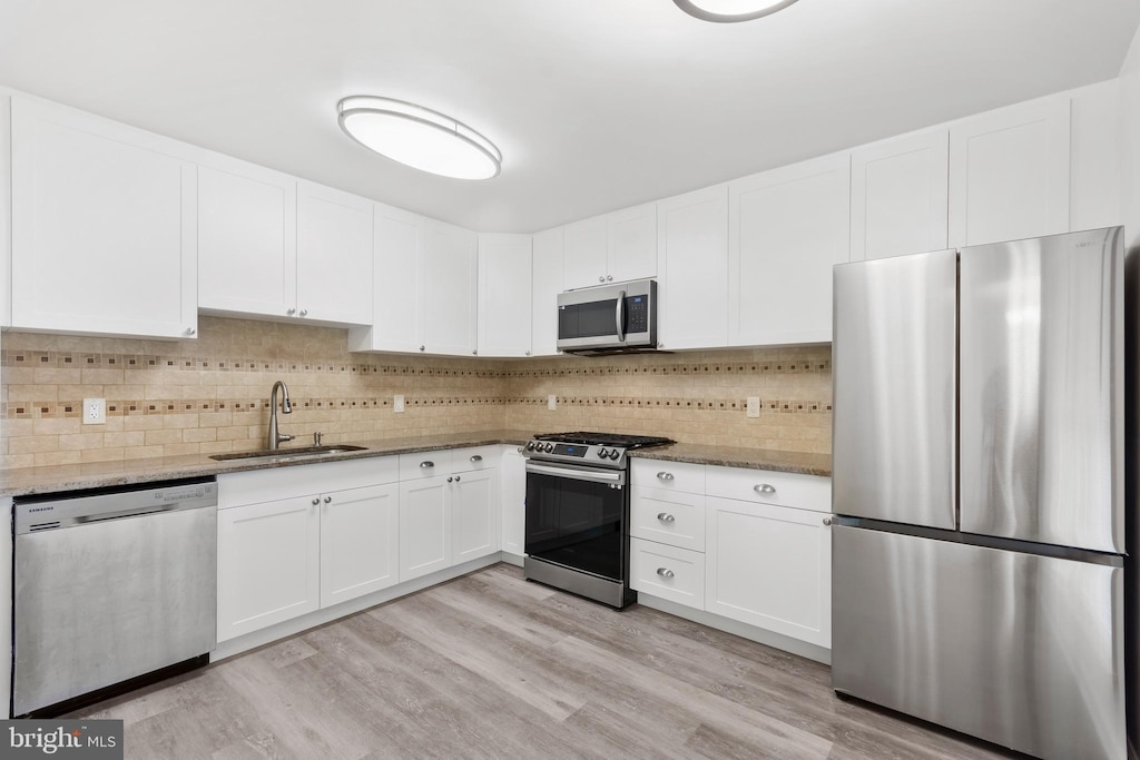 kitchen with light hardwood / wood-style floors, light stone countertops, sink, and appliances with stainless steel finishes