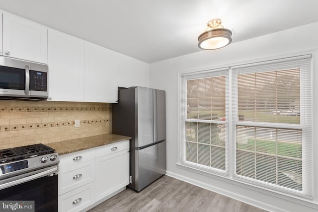 kitchen with light hardwood / wood-style flooring, decorative backsplash, dark stone countertops, white cabinetry, and stainless steel appliances