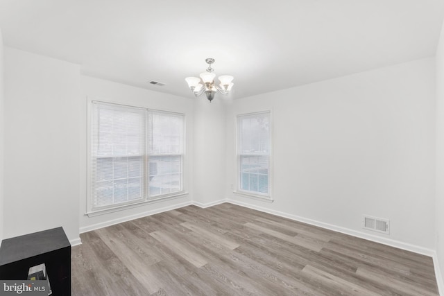 empty room featuring light wood-type flooring and a notable chandelier