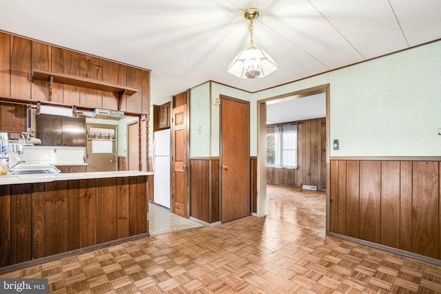 kitchen with pendant lighting, white fridge, kitchen peninsula, and wooden walls