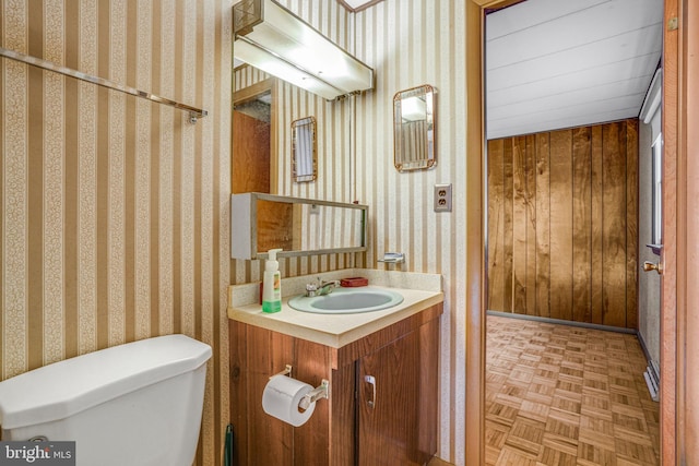 bathroom with parquet flooring, vanity, toilet, and wooden walls