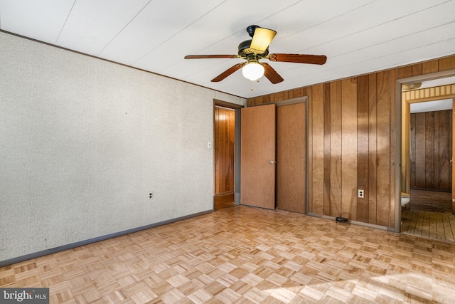 spare room with ceiling fan, light parquet flooring, and wood walls