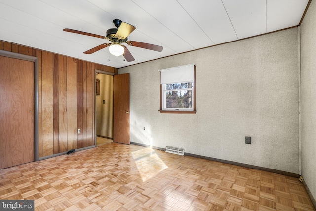 empty room with ceiling fan, wooden walls, and light parquet flooring