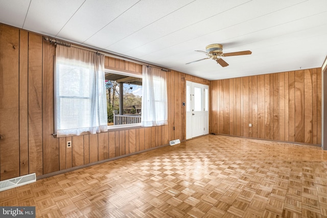 empty room featuring ceiling fan, wooden walls, and light parquet floors