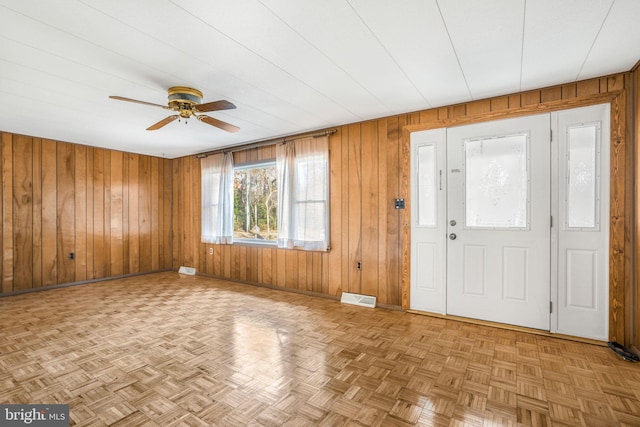 foyer entrance with wood walls, light parquet floors, and ceiling fan