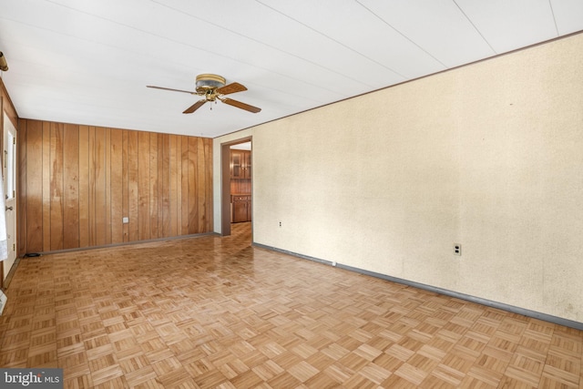 spare room with light parquet flooring, ceiling fan, and wood walls