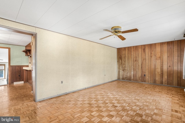 spare room with ceiling fan, wood walls, and light parquet floors