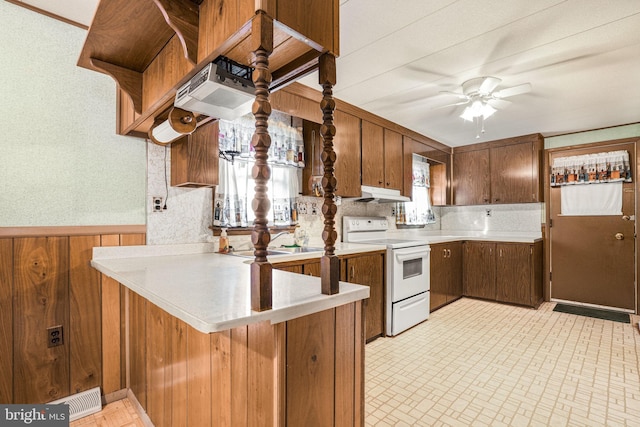 kitchen with ceiling fan, sink, white range with electric cooktop, kitchen peninsula, and wooden walls