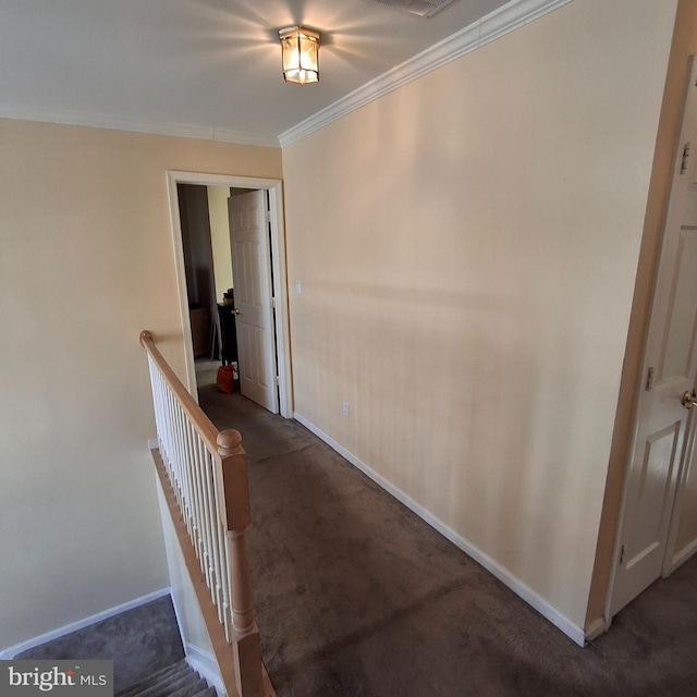 hall with ornamental molding and dark colored carpet