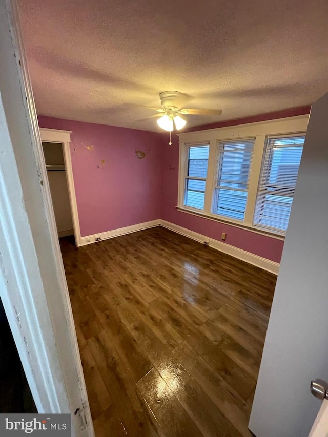 empty room featuring a textured ceiling, ceiling fan, and dark wood-type flooring