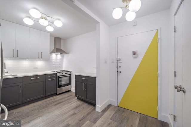 kitchen featuring wall chimney range hood, decorative backsplash, white cabinetry, light hardwood / wood-style flooring, and gas range