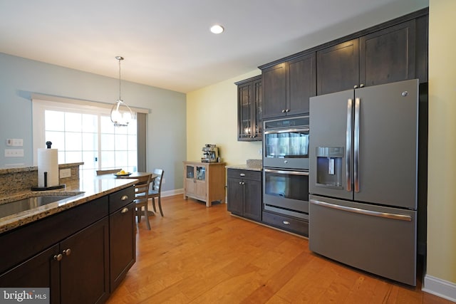 kitchen featuring hanging light fixtures, light wood-type flooring, light stone countertops, appliances with stainless steel finishes, and dark brown cabinets