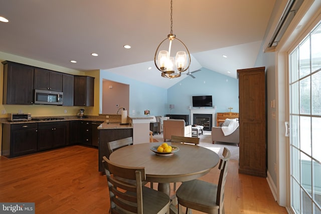 dining area with light hardwood / wood-style floors, vaulted ceiling, sink, and an inviting chandelier