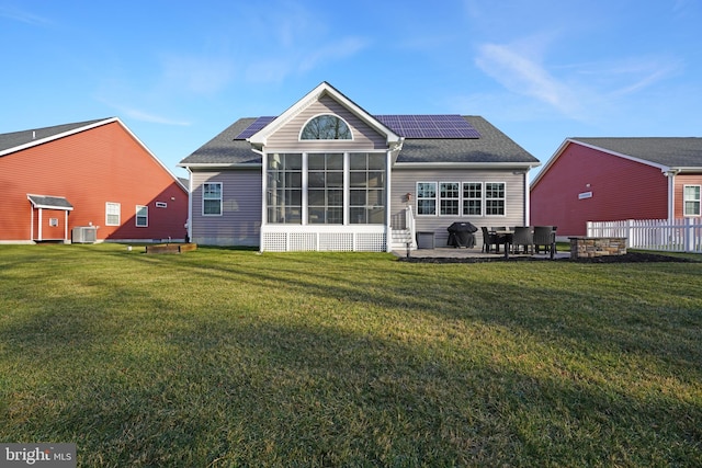 rear view of house featuring a sunroom, a yard, a patio, and solar panels