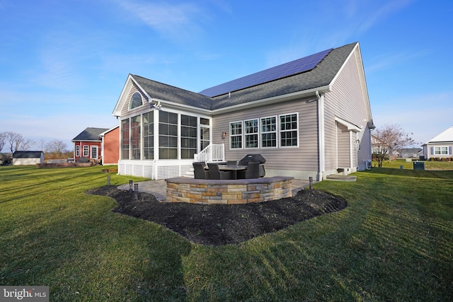 back of property featuring a patio area, a sunroom, a yard, and solar panels