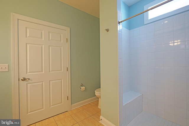 bathroom with tile patterned flooring, a tile shower, and toilet