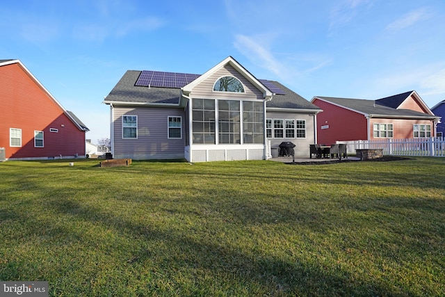 back of property with a sunroom, solar panels, a patio area, and a lawn