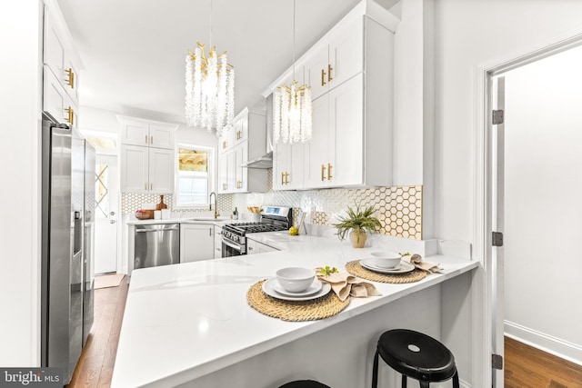 kitchen featuring kitchen peninsula, stainless steel appliances, white cabinets, hanging light fixtures, and a breakfast bar area