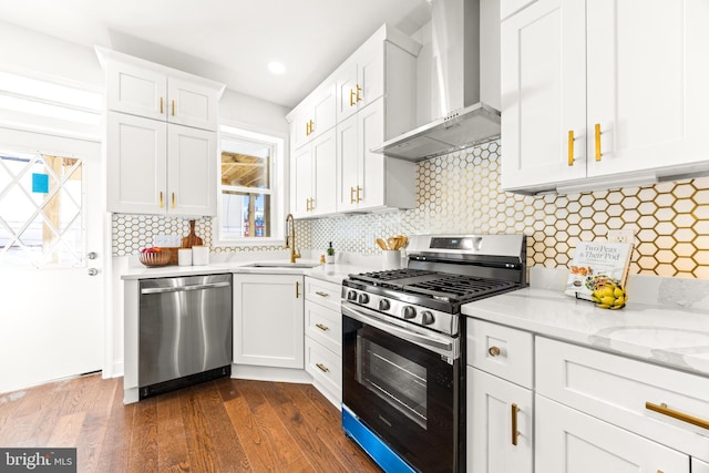 kitchen featuring appliances with stainless steel finishes, tasteful backsplash, sink, wall chimney range hood, and white cabinetry