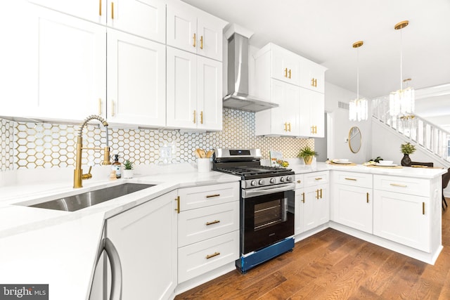 kitchen featuring sink, wall chimney exhaust hood, dark hardwood / wood-style floors, range with gas stovetop, and decorative light fixtures