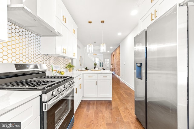 kitchen with stainless steel appliances, wall chimney range hood, backsplash, pendant lighting, and white cabinets