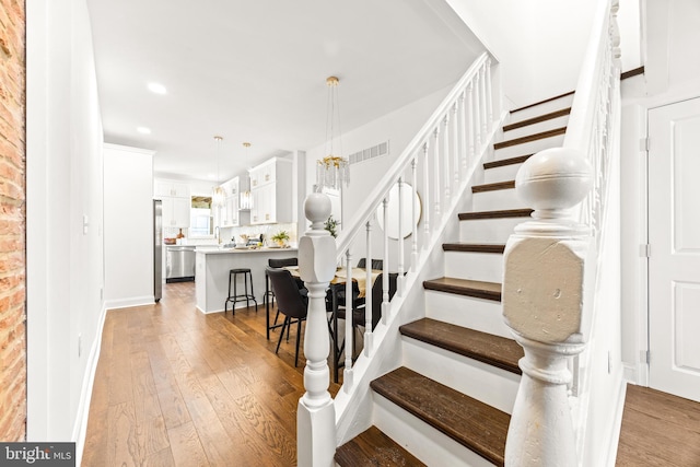 stairs with hardwood / wood-style flooring and an inviting chandelier