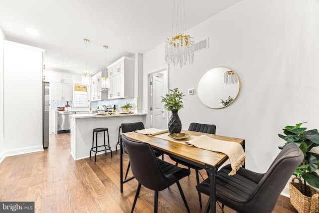 dining room featuring light wood-type flooring, a notable chandelier, and sink