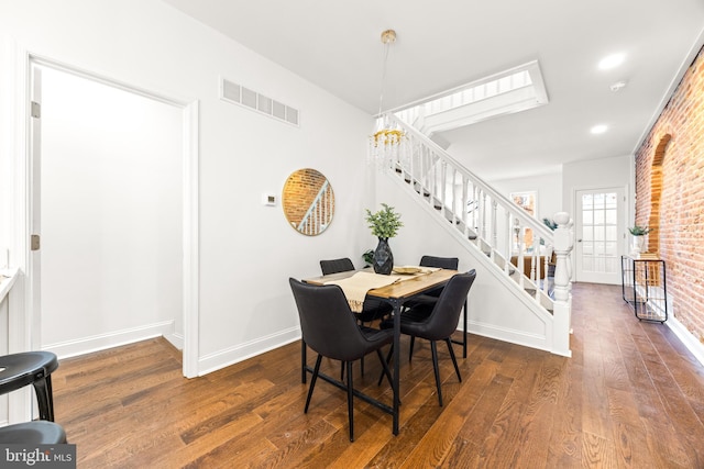 dining room with a chandelier, dark hardwood / wood-style floors, and brick wall