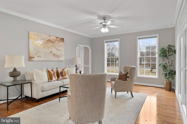 living room with arched walkways, wood-type flooring, ornamental molding, a ceiling fan, and baseboards