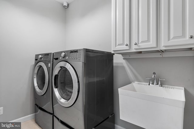 washroom with cabinet space, light tile patterned floors, baseboards, washing machine and clothes dryer, and a sink