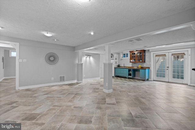 unfurnished living room with a textured ceiling, visible vents, baseboards, french doors, and indoor wet bar