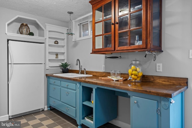 kitchen with open shelves, blue cabinetry, a sink, and freestanding refrigerator