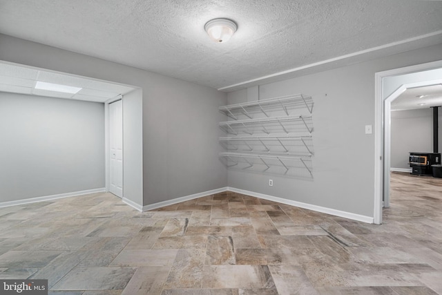 spare room with a wood stove, stone finish floor, a textured ceiling, and baseboards