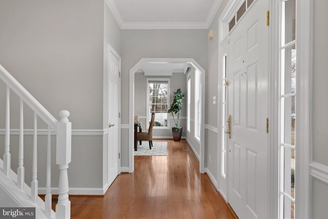 foyer featuring arched walkways, baseboards, wood-type flooring, stairway, and ornamental molding