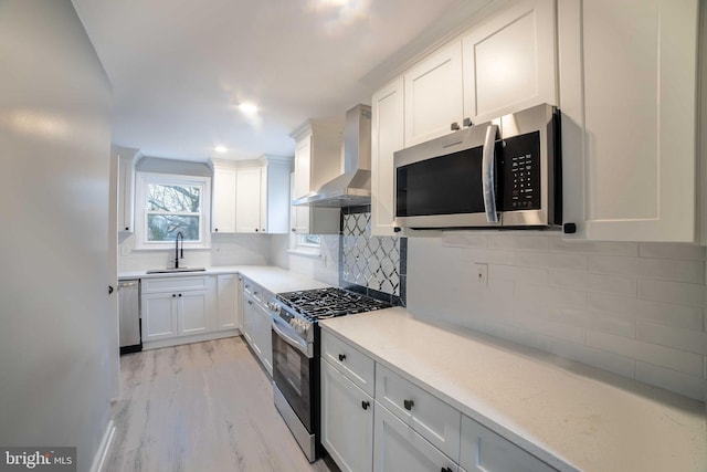 kitchen featuring sink, wall chimney exhaust hood, light wood-type flooring, white cabinetry, and stainless steel appliances