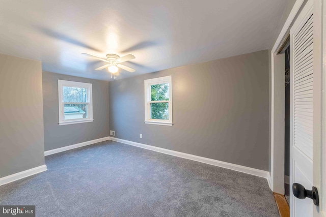 unfurnished bedroom with ceiling fan, dark carpet, and multiple windows