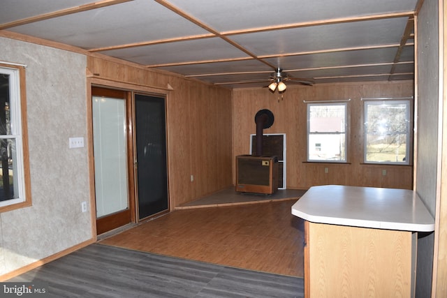 kitchen with a wood stove, ceiling fan, dark wood-type flooring, and wood walls