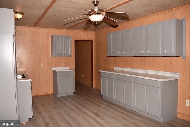 kitchen featuring gray cabinetry, wood walls, sink, ceiling fan, and light wood-type flooring