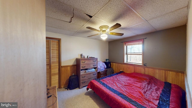 bedroom with carpet, a drop ceiling, ceiling fan, a closet, and wood walls