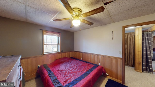 carpeted bedroom featuring ceiling fan, a drop ceiling, and wooden walls