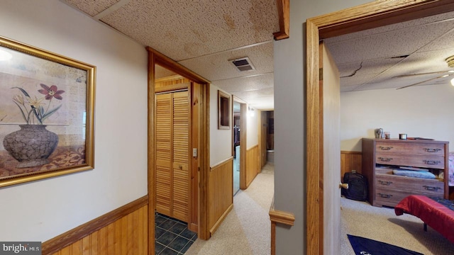 hall featuring carpet, a paneled ceiling, and wooden walls