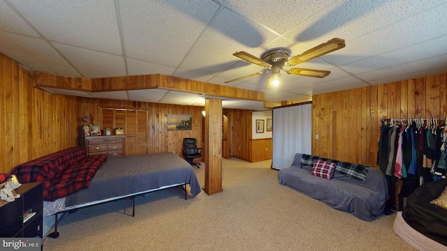 bedroom featuring ceiling fan, wood walls, and light carpet