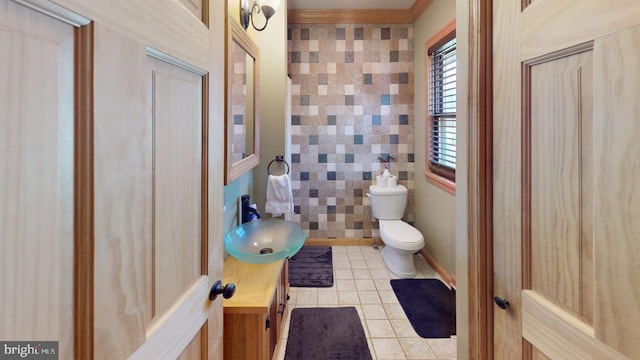 bathroom with tile patterned floors, crown molding, toilet, vanity, and tile walls