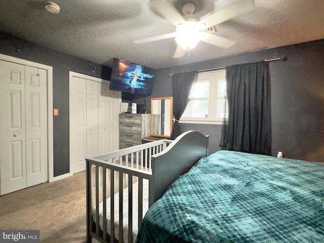 bedroom with ceiling fan, carpet floors, a textured ceiling, and two closets