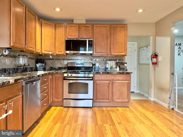 kitchen with decorative backsplash, stainless steel appliances, light hardwood / wood-style flooring, and dark stone countertops