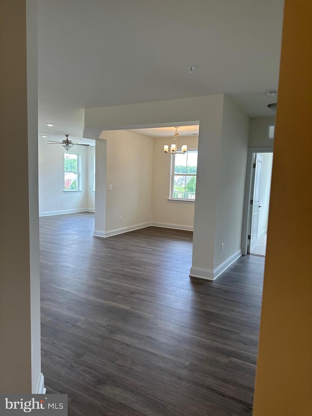 empty room with ceiling fan with notable chandelier and dark wood-type flooring