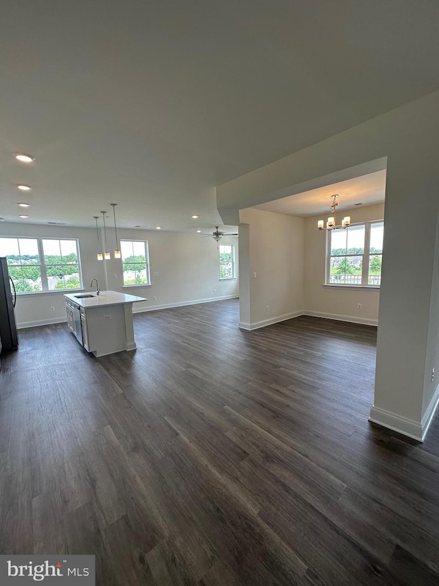 unfurnished living room featuring ceiling fan with notable chandelier, sink, a wealth of natural light, and dark wood-type flooring